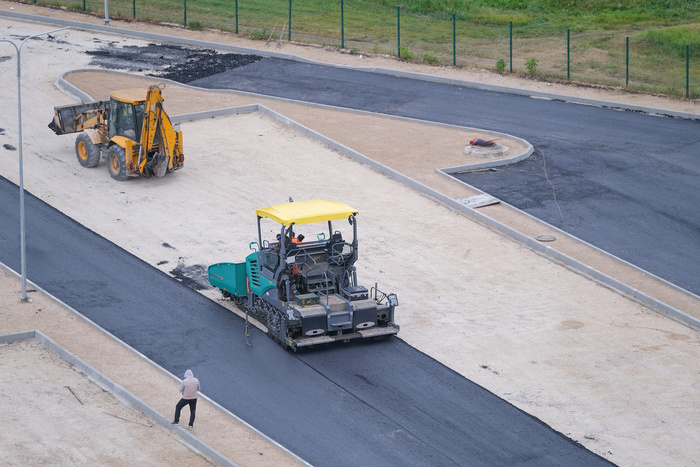 Worker, asphalt paving machine while lays asphalt for parking lot