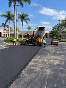 Trinity Asphalt Paving crew resurfacing a West Palm Beach shopping center parking lot with fresh asphalt and paving equipment.